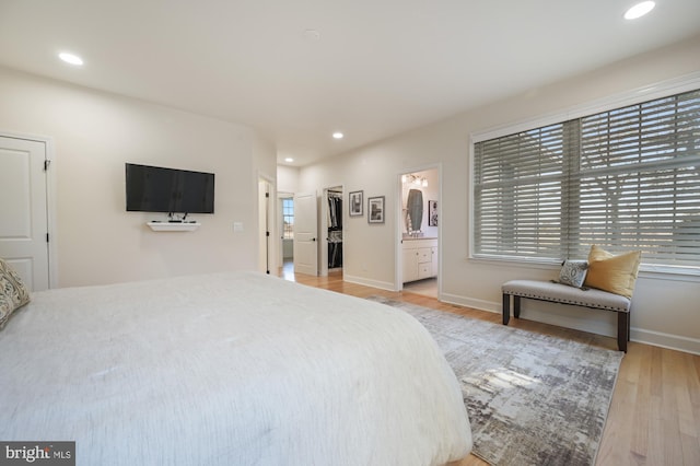 bedroom featuring a walk in closet, connected bathroom, hardwood / wood-style flooring, and multiple windows