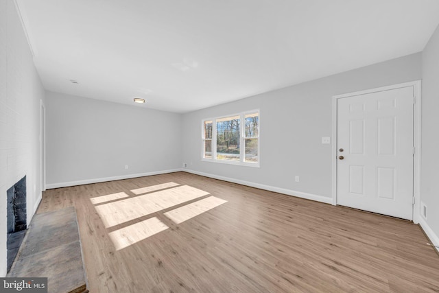 unfurnished living room featuring light wood-type flooring and a brick fireplace