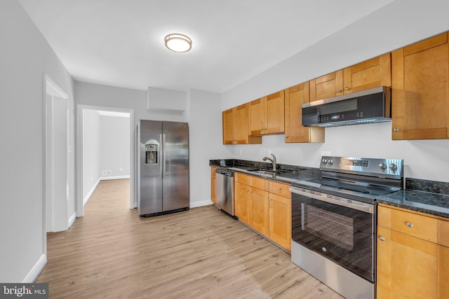 kitchen with sink, appliances with stainless steel finishes, light wood-type flooring, and dark stone countertops