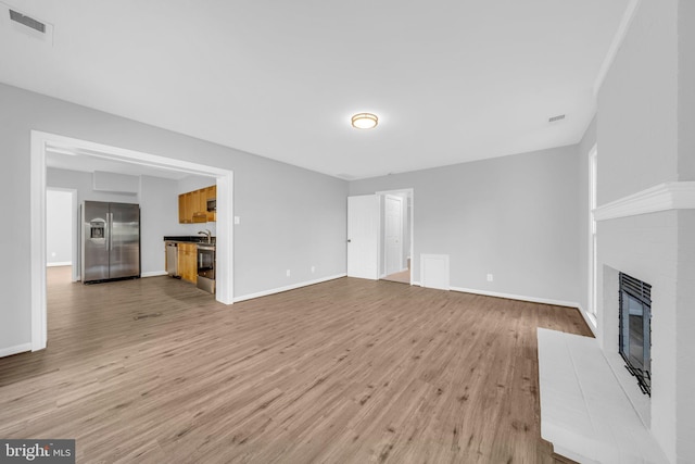 unfurnished living room featuring sink, a fireplace, and light hardwood / wood-style flooring