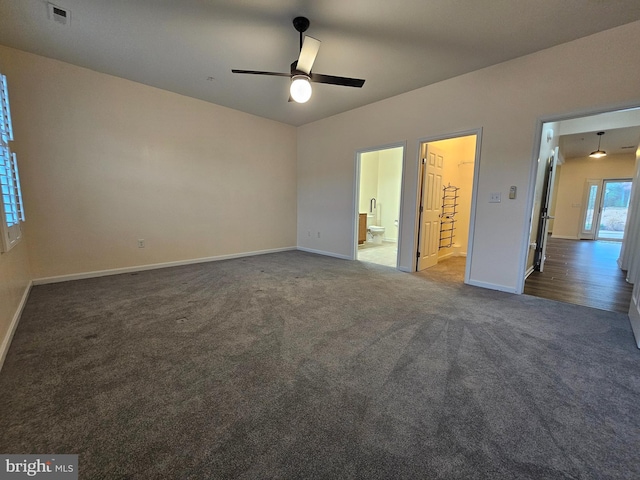 unfurnished bedroom featuring dark carpet, ensuite bath, and ceiling fan