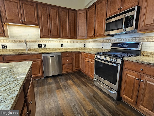 kitchen featuring sink, appliances with stainless steel finishes, tasteful backsplash, dark hardwood / wood-style flooring, and light stone counters