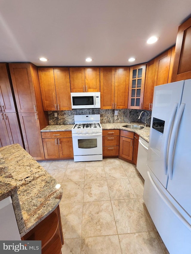 kitchen featuring white appliances, backsplash, light stone counters, and sink