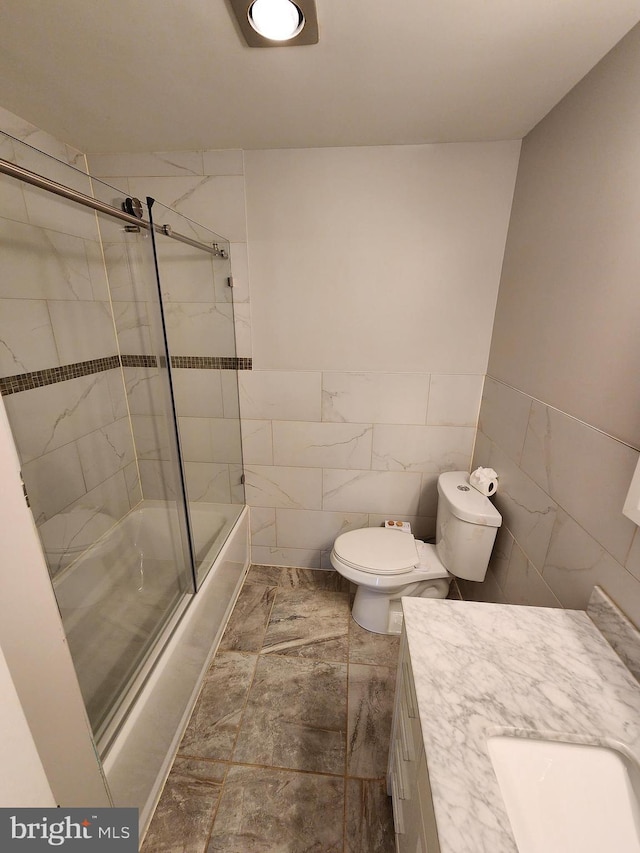 full bathroom with shower / bath combination with glass door, vanity, tile walls, and toilet