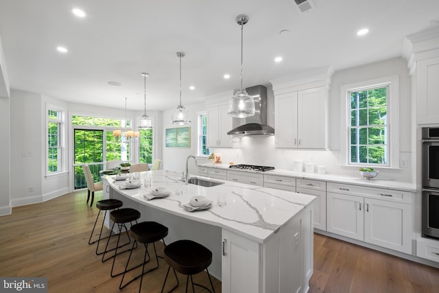 kitchen featuring sink, dark wood-type flooring, wall chimney range hood, an island with sink, and white cabinets