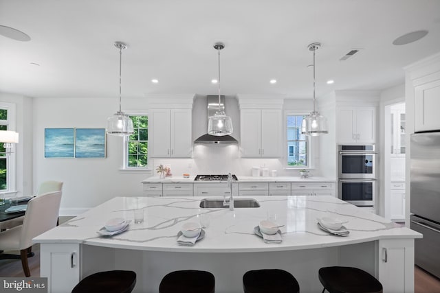 kitchen featuring a large island, hanging light fixtures, wall chimney exhaust hood, and stainless steel appliances