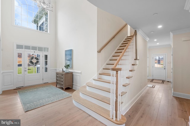 entryway with light wood-type flooring, ornamental molding, and a towering ceiling