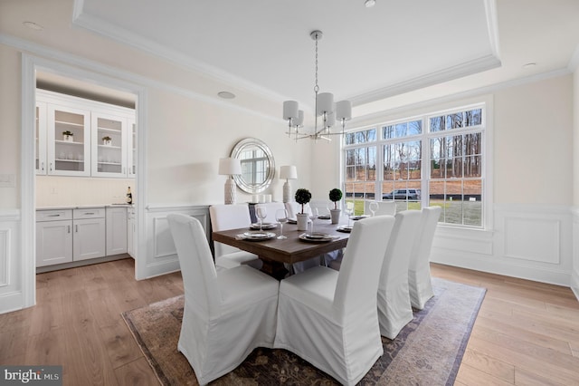 dining area featuring a raised ceiling, light hardwood / wood-style flooring, and a notable chandelier