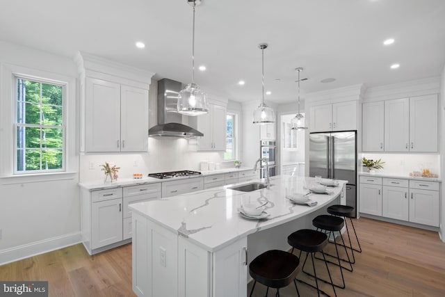 kitchen with an island with sink, light hardwood / wood-style floors, wall chimney exhaust hood, and sink