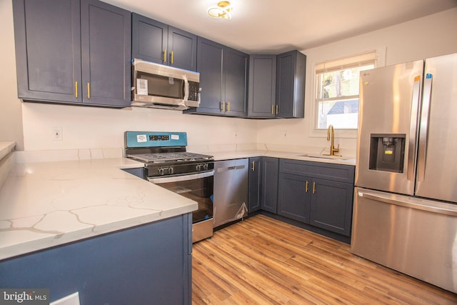 kitchen with light stone counters, sink, stainless steel appliances, and light hardwood / wood-style flooring