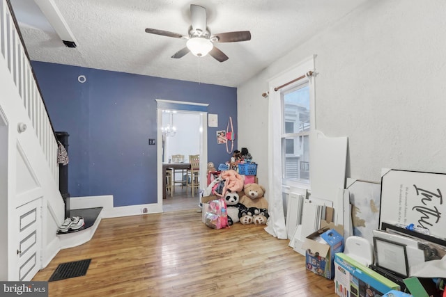 playroom featuring ceiling fan with notable chandelier, a textured ceiling, and light hardwood / wood-style flooring