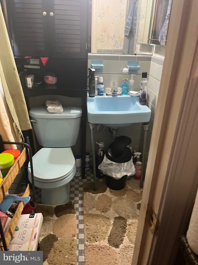 bathroom featuring toilet, tile walls, and sink