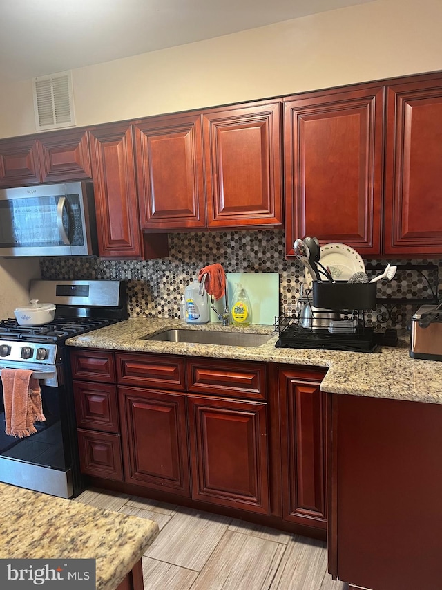 kitchen with decorative backsplash, light stone counters, sink, and appliances with stainless steel finishes