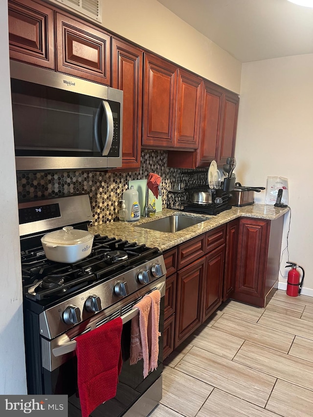 kitchen with stainless steel appliances, light stone counters, tasteful backsplash, and sink