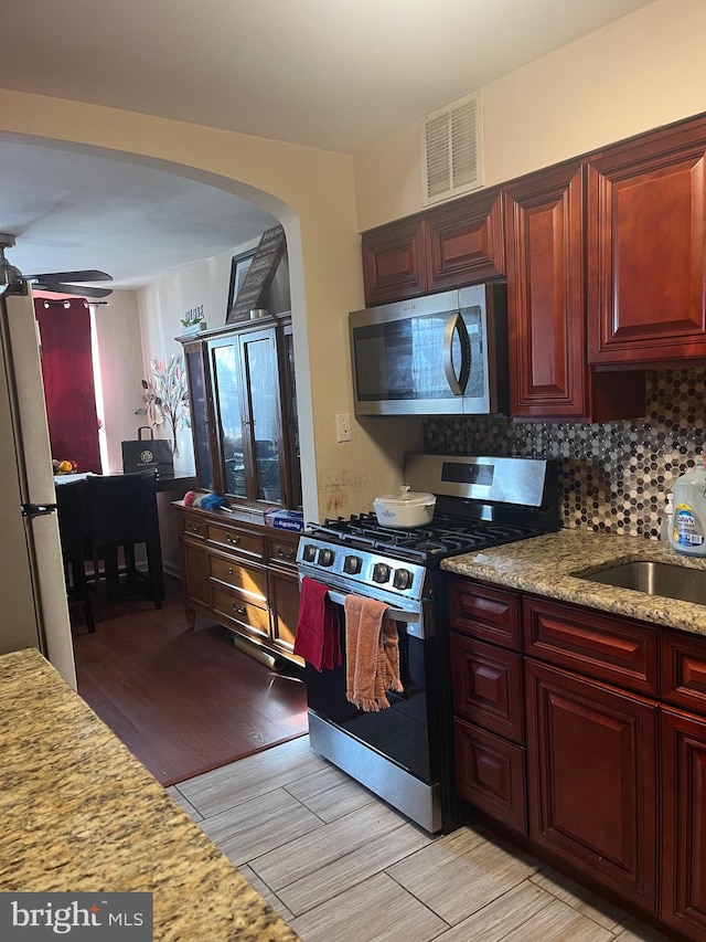 kitchen featuring light stone countertops, appliances with stainless steel finishes, backsplash, sink, and light hardwood / wood-style floors