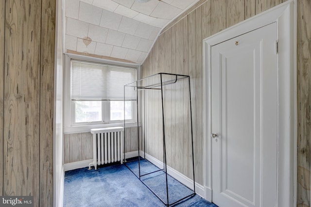 unfurnished bedroom with carpet flooring, radiator, wood walls, and vaulted ceiling