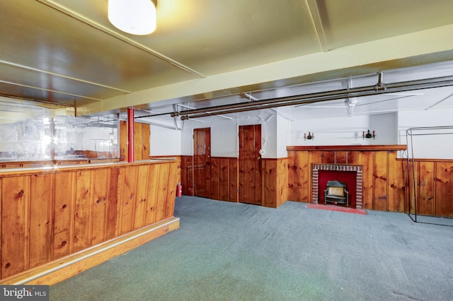 basement with carpet floors, a brick fireplace, and wooden walls