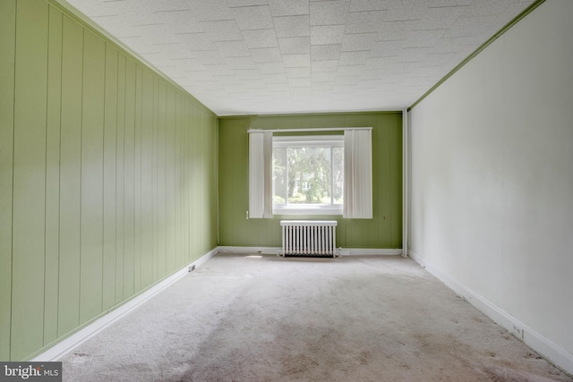 spare room featuring crown molding, radiator heating unit, light colored carpet, and wood walls