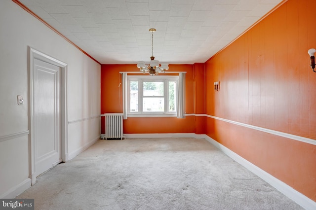 carpeted empty room with radiator heating unit, wooden walls, crown molding, and a notable chandelier