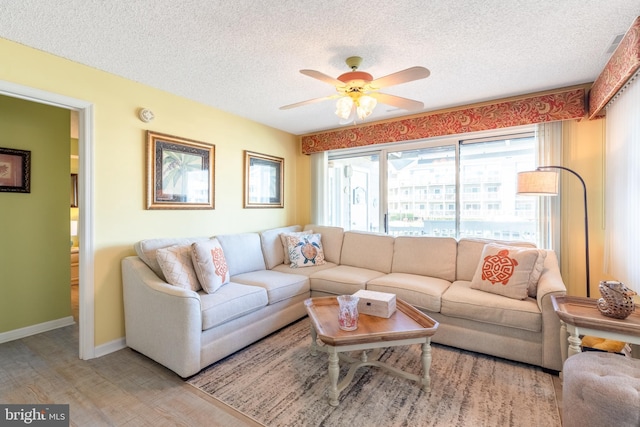 living room featuring ceiling fan, light hardwood / wood-style flooring, and a textured ceiling