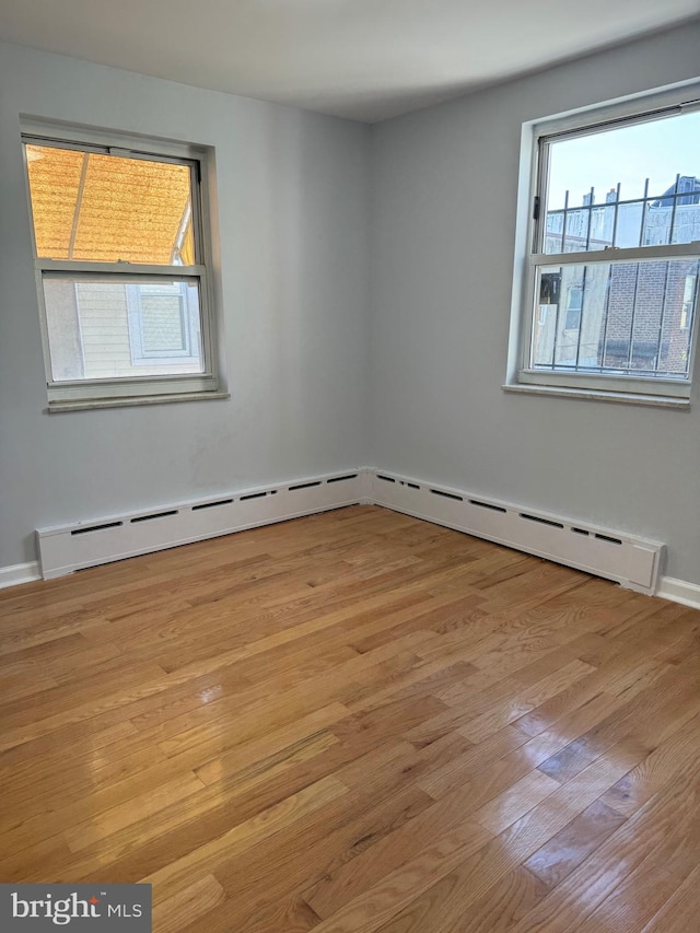 empty room with baseboard heating, light wood-type flooring, and plenty of natural light