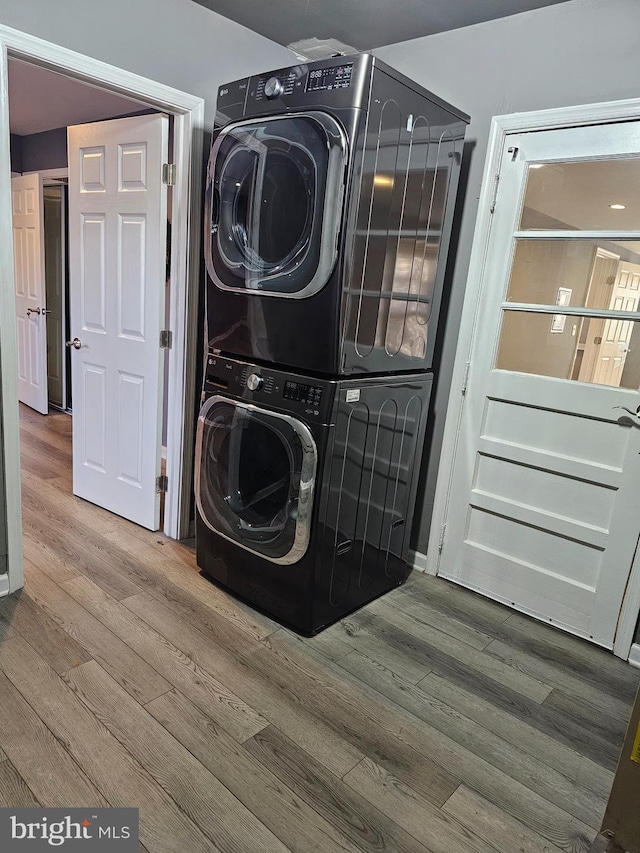 clothes washing area featuring wood-type flooring and stacked washer and clothes dryer