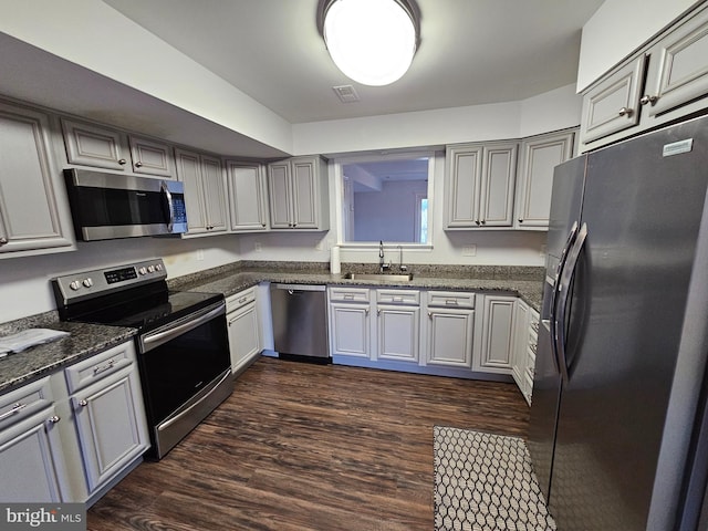 kitchen with gray cabinetry, sink, dark stone countertops, dark hardwood / wood-style flooring, and stainless steel appliances