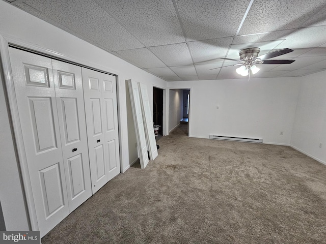 basement featuring a paneled ceiling, ceiling fan, carpet, and a baseboard heating unit