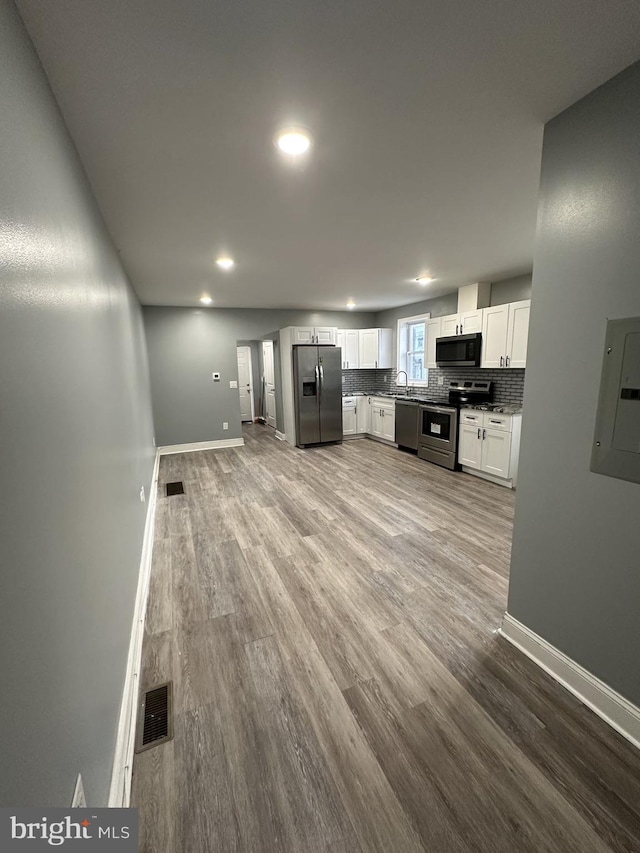 kitchen with backsplash, electric panel, white cabinets, wood-type flooring, and stainless steel appliances