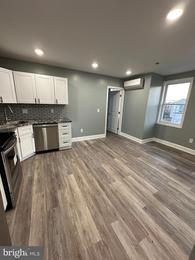 kitchen with sink, an AC wall unit, appliances with stainless steel finishes, white cabinets, and hardwood / wood-style flooring