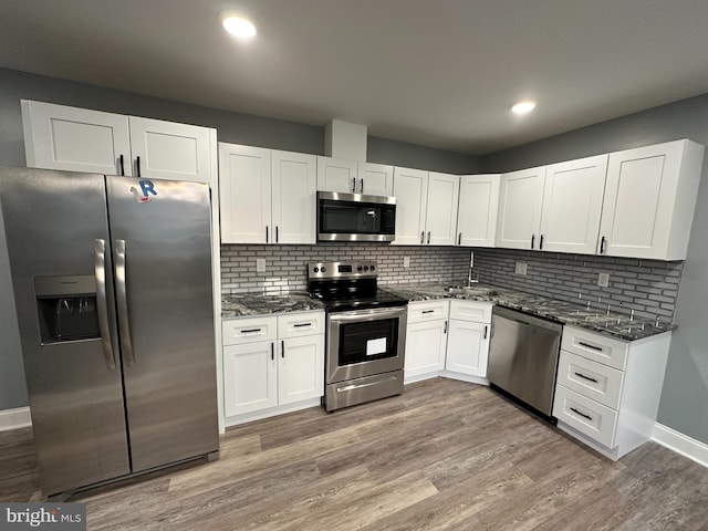 kitchen featuring dark stone countertops, white cabinets, stainless steel appliances, and light hardwood / wood-style floors