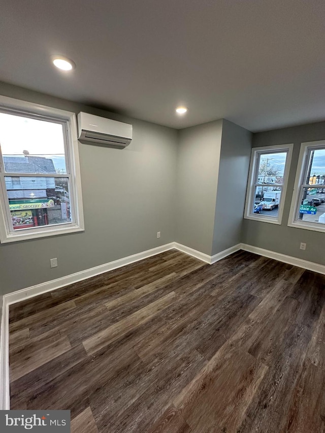 spare room with dark hardwood / wood-style flooring, a wall unit AC, and a healthy amount of sunlight