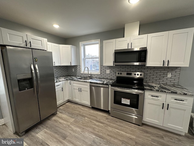 kitchen with white cabinets, appliances with stainless steel finishes, dark stone counters, and sink