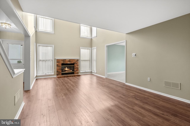 unfurnished living room featuring a towering ceiling, wood-type flooring, and a brick fireplace