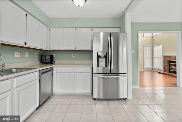 kitchen featuring appliances with stainless steel finishes, light wood-type flooring, a fireplace, sink, and white cabinets