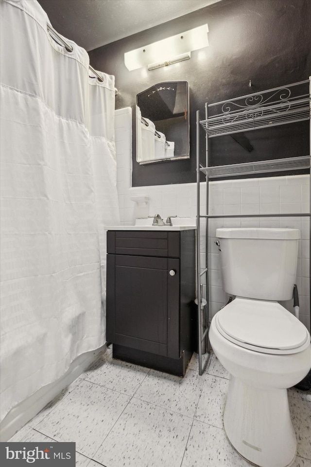 bathroom with vanity, toilet, and tile walls