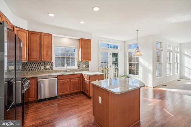 kitchen with decorative backsplash, appliances with stainless steel finishes, light stone counters, sink, and hanging light fixtures