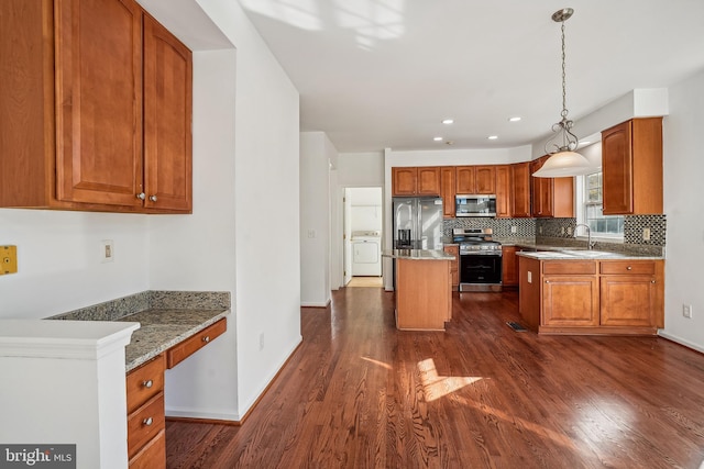 kitchen featuring stainless steel appliances, dark hardwood / wood-style floors, washer / clothes dryer, a kitchen island, and hanging light fixtures