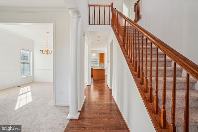 stairs with hardwood / wood-style floors, an inviting chandelier, ornate columns, and ornamental molding