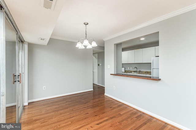 unfurnished dining area with crown molding, sink, wood-type flooring, and an inviting chandelier