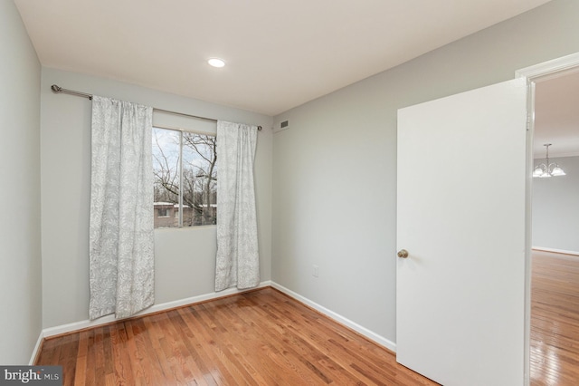 empty room with hardwood / wood-style floors and a notable chandelier