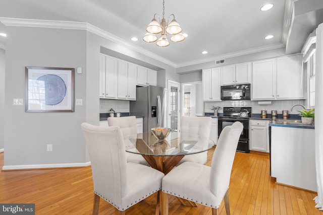 dining space with sink, light hardwood / wood-style flooring, crown molding, and a chandelier