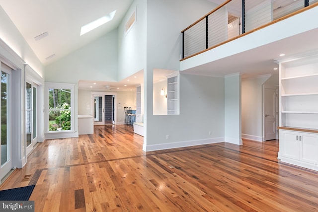 unfurnished living room featuring a skylight, light wood finished floors, visible vents, a high ceiling, and baseboards