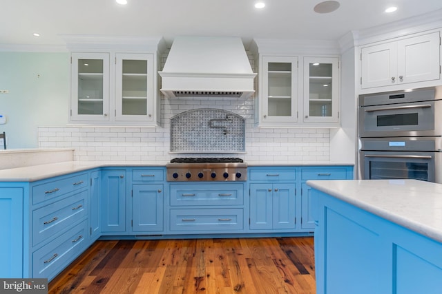 kitchen with stainless steel appliances, premium range hood, light countertops, glass insert cabinets, and crown molding