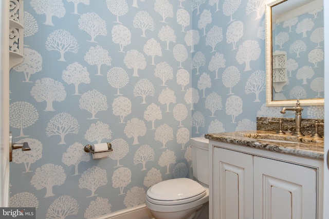 bathroom featuring toilet, wallpapered walls, and vanity