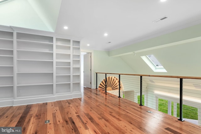 empty room featuring lofted ceiling with skylight, wood-type flooring, visible vents, and a healthy amount of sunlight