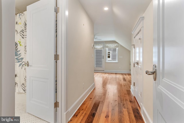 hallway featuring vaulted ceiling, light wood-style floors, and baseboards