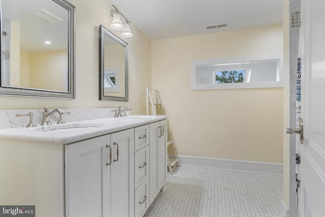 bathroom with double vanity, baseboards, visible vents, and a sink