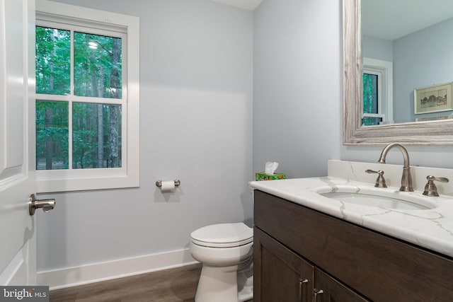 half bathroom featuring vanity, wood finished floors, toilet, and baseboards