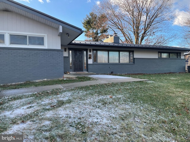 view of front of property featuring brick siding, metal roof, a chimney, and a front lawn